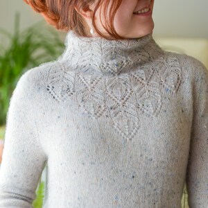 Könnte beinhalten: Ein weißer Strickpullover mit einem zarten Spitzenmuster am Ausschnitt. Der Pullover hat eine gesprenkelte Textur und einen hohen Kragen.