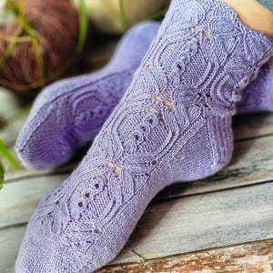 May include: A pair of lavender knitted socks with a lacy pattern. The socks are made with a fine yarn and have a delicate, feminine look.
