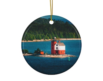 May include: A red and white lighthouse stands on a small island in a blue body of water. The lighthouse is surrounded by green trees and a sandy beach.