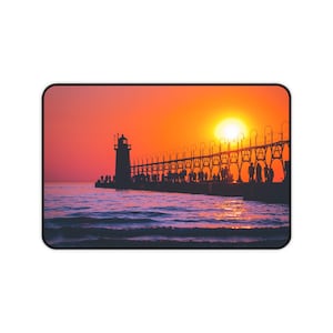 May include: A silhouette of a lighthouse and a pier with people standing on it against a vibrant orange and pink sunset sky.