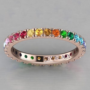 May include: Rose gold ring with a full band of colourful gemstones in a rainbow pattern. The ring features pink, red, yellow, orange, green, and blue stones. The word "JEWELACY" is engraved on the inside of the ring.