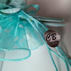 Könnte beinhalten: Eine hellblaue Tülltasche mit weißen Punkten und einem silbernen Etikett mit der Aufschrift "CB Schipaani & Bella".