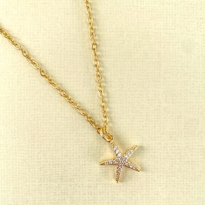 Puede incluir: Un collar de cadena dorada con un peque&ntilde;o colgante de estrella de mar brillante.