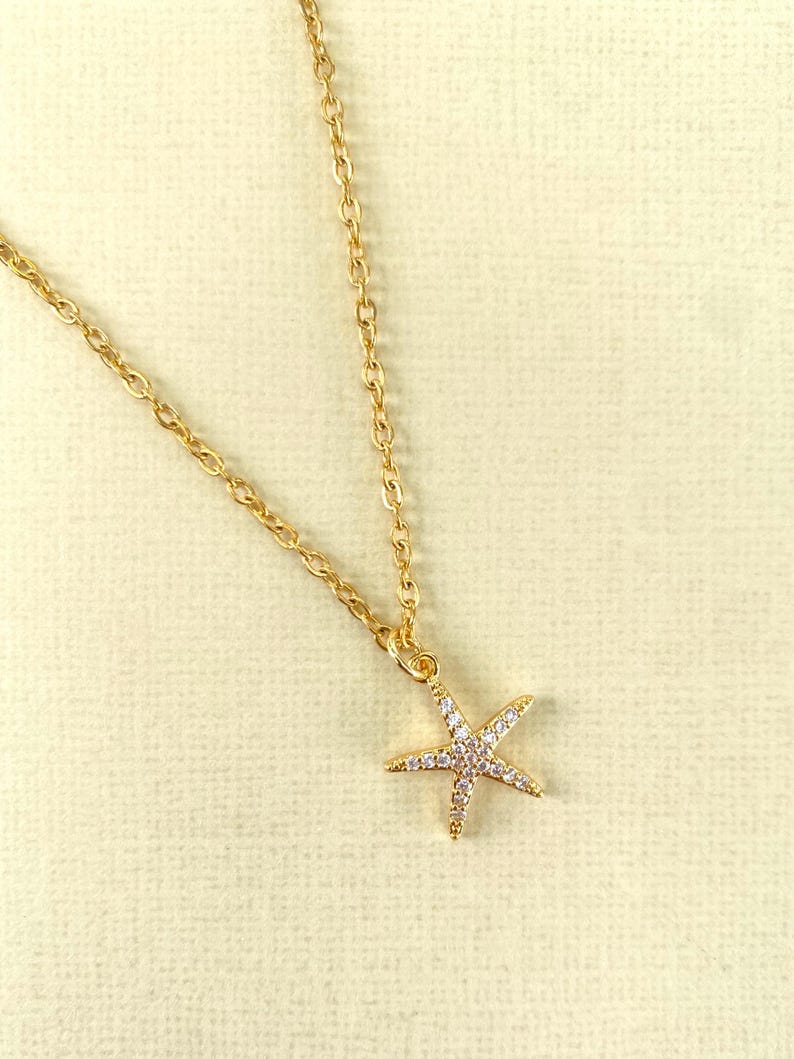 Puede incluir: Un collar de cadena dorada con un peque&ntilde;o colgante de estrella de mar brillante.