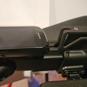 May include: A black Garmin cycling computer mounted on a black handlebar with a black mount.