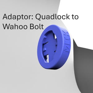 Op de afbeelding: Een blauwe plastic adapter voor een fietscomputer. Hij is ontworpen om te passen op een Quadlock-bevestiging en een Wahoo Bolt-computer. De adapter heeft een ronde vorm met een verhoogd middengedeelte en een klein gaatje in het midden.