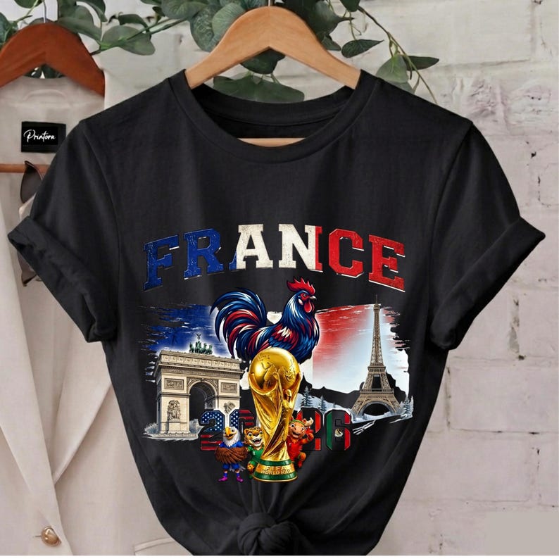 May include: Black t-shirt with a graphic featuring the word "FRANCE" in blue and red, a rooster, the Eiffel Tower, Arc de Triomphe, and a golden trophy. The design incorporates elements of the French flag.