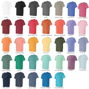 May include: A collection of short-sleeved t-shirts in various colors, including white, black, grey, and blue. Each shirt is displayed with its color name underneath, such as "White," "Black," and "Flo Blue." The shirts are made of a soft material.