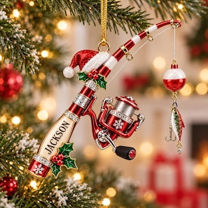 May include: A red and white fishing rod ornament featuring a Santa hat, holly leaves, and berries. The rod is personalized with the name JACKSON in black text. It includes a spinning reel, a red and white bobber, and a small fish lure.