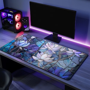 May include: A blue and purple stained glass design desk mat with white lotus flowers. The mat is on a wooden desk with a computer monitor and speakers.