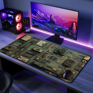 May include: A rectangular mouse mat featuring a circuit board design in green, brown, and grey. A black computer mouse sits on the mat. A computer monitor, speakers, and a desktop computer are also visible.