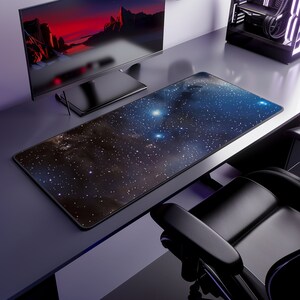 May include: A rectangular desk mouse pad with a cosmic design featuring a dark blue and brown nebula with white stars. The pad is on a gray desk, next to a computer monitor and a black computer tower.