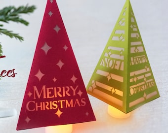 Può includere: Dieci modelli di alberi di Natale per l'artigianato. L'immagine mostra due alberi di Natale di carta, uno rosso con il testo "Buon Natale" e l'altro verde con il testo "Buon Natale". Entrambi gli alberi hanno una luce all'interno.