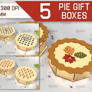 May include: Five pie-shaped gift boxes with different designs. The boxes are made of wood and have a natural finish. The designs include a pie with a lattice crust, a pie with a solid crust, a pie with a leaf design, and a pie with the words "Apple of My Eye".