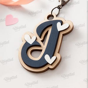May include: Wooden letter "J" keychain with a navy blue center and light wood border, adorned with white heart accents. The keychain is attached to a metal clasp. The image also includes heart-shaped cutouts and the text "SUITED FOR ANY MATERIAL THICKNESS".
