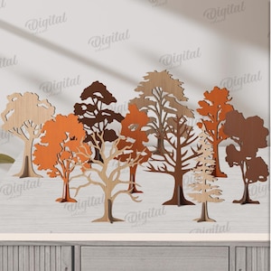 Può includere: Una collezione di dieci modelli di alberi in legno in varie tonalità di marrone e arancione. Gli alberi sono tagliati da materiale di 3 mm di spessore. L'immagine include il testo "10 DESIGNS", "MATERIAL WIDTH: 3 MM" e "DIGITAL DOWNLOAD".