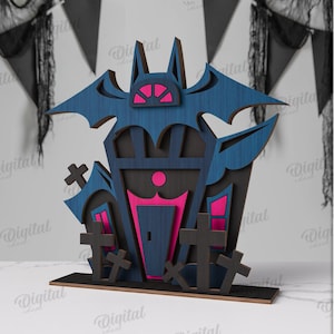 May include: A Halloween wooden decoration of a haunted house with a bat, in blue with pink accents and black crosses. The material width is 3 mm. The house is made of wood.