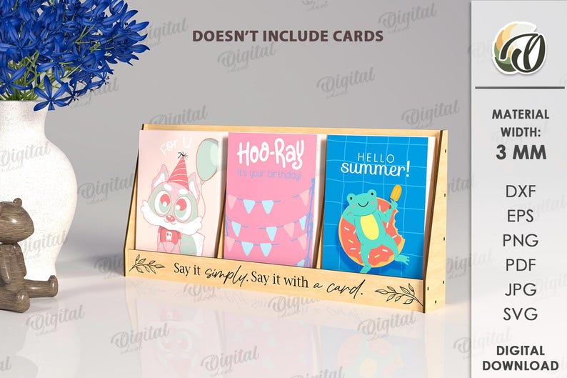 May include: A wooden card display stand holding three greeting cards with colorful illustrations. The cards feature a cartoon fox, pink birthday decorations, and a frog with a popsicle. The stand has the text "Say it simply. Say it with a card."