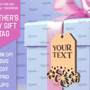 May include: A light blue gift box with a pink ribbon and a wooden gift tag with the text "YOUR TEXT" and a floral design. The tag is hanging from the ribbon. The box is on a purple background with the text "MOTHER'S DAY GIFT TAG" on a pink background.