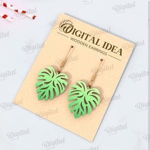 May include: A digital download of a pair of wooden earrings featuring a green monstera leaf design. The earrings are shown on a brown card with the text "Digital Idea Wooden Earrings".