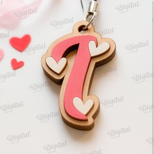 May include: Wooden letter "T" pendant with a pink center and heart accents. The pendant is layered and has a natural wood grain finish. Small red and pink heart-shaped cutouts are scattered around the pendant. The image also includes the text "SUITED FOR ANY MATERIAL THICKNESS" and "DIGITAL DOWNLOAD".
