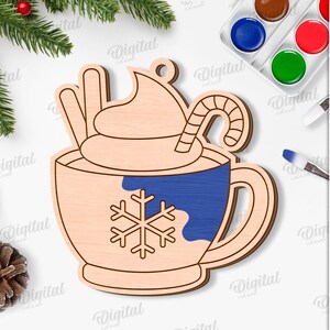 May include: Wooden Christmas ornament in the shape of a hot chocolate mug with whipped cream, a candy cane, and a snowflake design. The mug has a blue section and is surrounded by festive decorations and text that says "SUITED FOR ANY MATERIAL THICKNESS".
