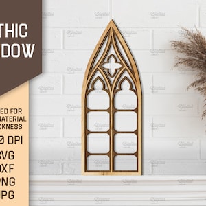 May include: A wooden cutout of a gothic window with a pointed arch and multiple panes. The window is on a white brick wall with a dried grass plant in a white vase.