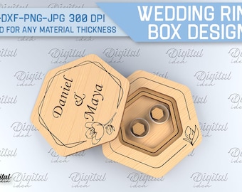 May include: Wooden wedding ring box design with the names "Daniel & Maya" engraved on the lid. The box is open, revealing two ring holders. The design includes floral accents and the text "WEDDING RING BOX DESIGN".