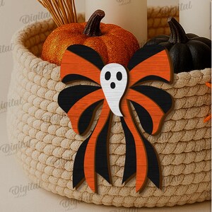 K&ouml;nnte beinhalten: Eine Halloween-Holzschleife mit Geisterausschnitt in einem geflochtenen Korb mit K&uuml;rbissen. Die Schleife hat schwarz-orange Streifen. Der Korb enth&auml;lt einen kleinen orangefarbenen K&uuml;rbis und einen schwarzen K&uuml;rbis. Auf der Seite steht "SUITED FOR ANY MATERIAL THICKNESS".