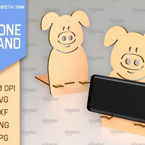 May include: A wooden phone stand shaped like a pig. The stand is 3 mm thick and is designed to hold a smartphone upright. The stand is made of light brown wood and has a simple design.