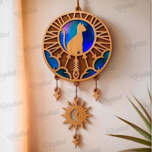 Peut inclure: D&eacute;coration murale en bois sur le th&egrave;me du chat, avec un design circulaire. La silhouette du chat est au centre, entour&eacute;e d'un fond bleu et violet. Le design comprend un soleil et une lune en bas, avec des &eacute;l&eacute;ments d&eacute;coratifs suspendus. Le texte &agrave; droite dit "SUITED FOR ANY MATERIAL THICKNESS".