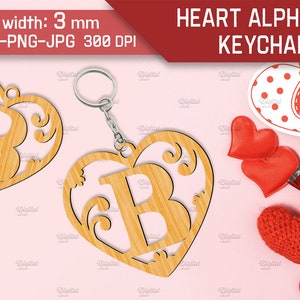 May include: A wooden heart-shaped keychain with a decorative letter B inside. The keychain is made of light brown wood and has a silver ring for attaching keys. The background is pink.