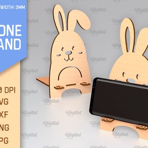 May include: A wooden phone stand shaped like a bunny rabbit. The stand is 3mm thick and is available in SVG, DXF, PNG, and JPG formats. The stand is designed to hold a smartphone upright.