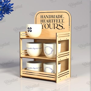 May include: A wooden display shelf with three levels, holding several white ceramic cups with blue floral designs. The top of the shelf has the words "HANDMADE. HEARTFELT. YOURS." etched into the wood.