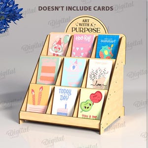 May include: A wooden greeting card display stand with nine slots, holding various colorful cards. The stand has a curved top with the text "ART WITH A PURPOSE". The material width is 3 mm.