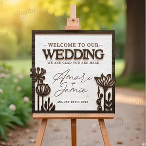 May include: A wooden wedding sign on an easel. The sign reads "WELCOME TO OUR WEDDING" with the names "Amari & Jamie" and the date "August 20th, 2026". Decorative floral cutouts frame the sign. The sign is displayed outdoors.