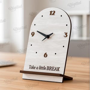 K&ouml;nnte beinhalten: Eine Holz-Schreibtischuhr mit hellem Holzmaserungs-Finish. Das Zifferblatt hat schwarze Zeiger und braune Ziffern. Auf der Basis der Uhr steht "Take a little BREAK". Die Uhr ist 3 mm breit.