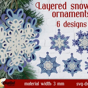 Könnte beinhalten: Geschichtete Schneeflocken-Ornamente in verschiedenen Designs. Die Ornamente bestehen aus geschichtetem Holz in Blau- und Weißtönen. Der Text "Layered snowflake ornaments 6 designs" ist sichtbar. Materialbreite: 3 mm.