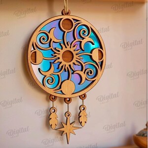 Peut inclure: D&eacute;coration murale c&eacute;leste en bois avec un motif de soleil, de lunes et d'&eacute;toiles. La pi&egrave;ce en bois d&eacute;coup&eacute;e au laser a un fond iris&eacute; color&eacute;. Des plumes d&eacute;coratives et une &eacute;toile pendent du bas. T&eacute;l&eacute;chargement num&eacute;rique.