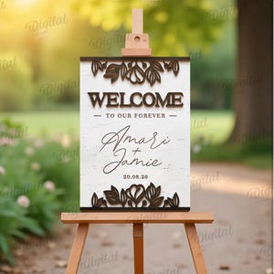 May include: A wooden welcome sign on an easel, featuring the words "WELCOME TO OUR FOREVER" and the names "Amari & Jamie" with the date 20.08.26. The sign has a floral design and is set against a blurred outdoor background.