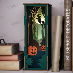 May include: A green and brown Halloween-themed decorative lantern with a witch flying in front of a full moon. The lantern features a forest scene with pumpkins and trees. A black spider sits on a stack of books. The text "HOUSEHOLD DECORATES" is visible.