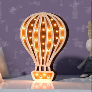 Puede incluir: Un globo aerostático de madera con bombillas, un diseño popular para una guardería o una habitación infantil. El globo es de color marrón claro y tiene un contorno blanco. Las bombillas son de color amarillo cálido. El globo está sentado sobre una superficie blanca.