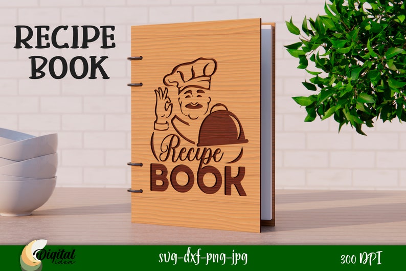 Może przedstawiać: Drewniana okładka książki kucharskiej z kresk&oacute;wkowym kucharzem trzymającym tacę. Tekst "Recipe Book" jest napisany ozdobnym fontem.
