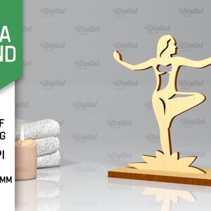 Peut inclure: Un support de yoga en bois avec une d&eacute;coupe d'une femme en position de yoga. Le support a une &eacute;paisseur de 3 mm et est con&ccedil;u pour &ecirc;tre utilis&eacute; avec une image de 300 DPI. Le support est sur une surface grise avec une serviette blanche et une bougie.