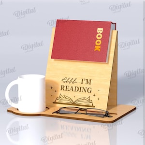 Może przedstawiać: Drewniany stojak na książki z czerwoną książką i białym kubkiem. Stojak ma napis "Shhh... I'M READING" i ilustrację otwartej książki. Stojak ma 3 mm szerokości i zawiera parę okularów.