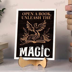 K&ouml;nnte beinhalten: Ein Holzschild mit dem Text "OPEN A BOOK, UNLEASH THE MAGIC" in wei&szlig;en Buchstaben. Das Schild zeigt ein goldenes Ph&ouml;nix-Design &uuml;ber einem offenen Buch. Das Schild ist 3 mm breit und wird auf einem Holzst&auml;nder pr&auml;sentiert.