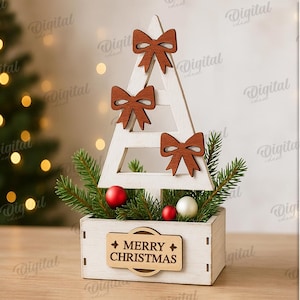 May include: A white wooden Christmas tree decoration with three brown bow accents. The tree sits in a white box with greenery, red and white ornaments, and a "MERRY CHRISTMAS" sign. The material width is 3 mm.
