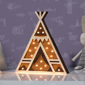 Può includere: Una luce notturna in legno a forma di teepee con finitura in legno marrone e contorno bianco. Il teepee ha una serie di piccole luci rotonde bianche all'interno. Il teepee è appoggiato su una superficie bianca.