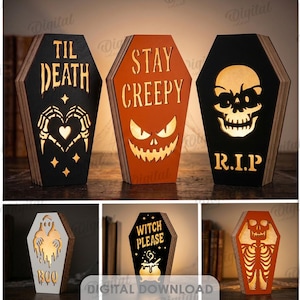 May include: A collection of ten coffin-shaped wooden decorative signs featuring cut-out designs including skulls, ghosts, and text such as TIL DEATH, STAY CREEPY, R.I.P, LET ME OUT, BOO, and WITCH PLEASE, illuminated from within with a warm light.
