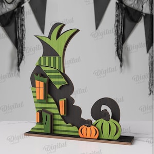 May include: A wooden Halloween decoration depicting a witch's hat, a house with orange windows, and two pumpkins. The decoration is made of layered wood and painted in green, black, and orange. The width is 3 mm.